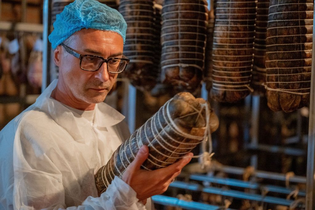 Cosa significa davvero artigianale? Operatore che controlla la stagionatura di un salume in cantina durante il processo produttivo